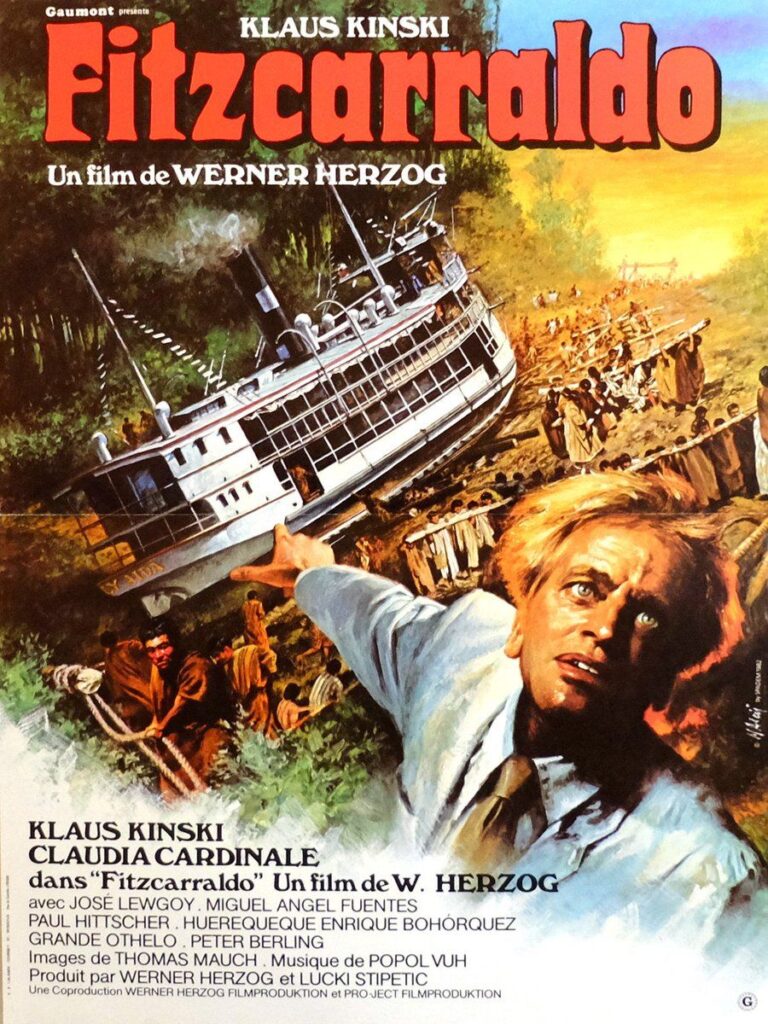 The poster for Fitzcarraldo; Klaus Kinsky turns wildly to the viewer, pointing behind him to a boat being dragged up a hill by numerous indigenous people